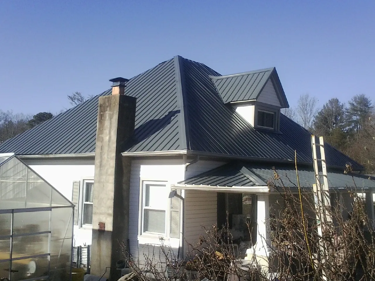 Dark blue standing seam metal roof on a white farmhouse with dormer — Slate & Tile Roof Repair by Roofing Brothers in Saint Hedwig