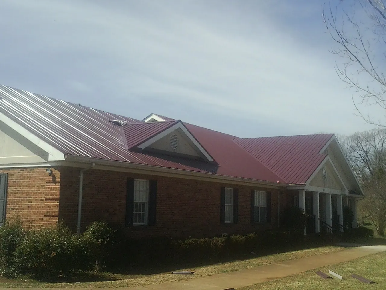 Red metal roof with gabled entries on a long brick building, from a Hail Damage Roof Repair job in Saint Hedwig