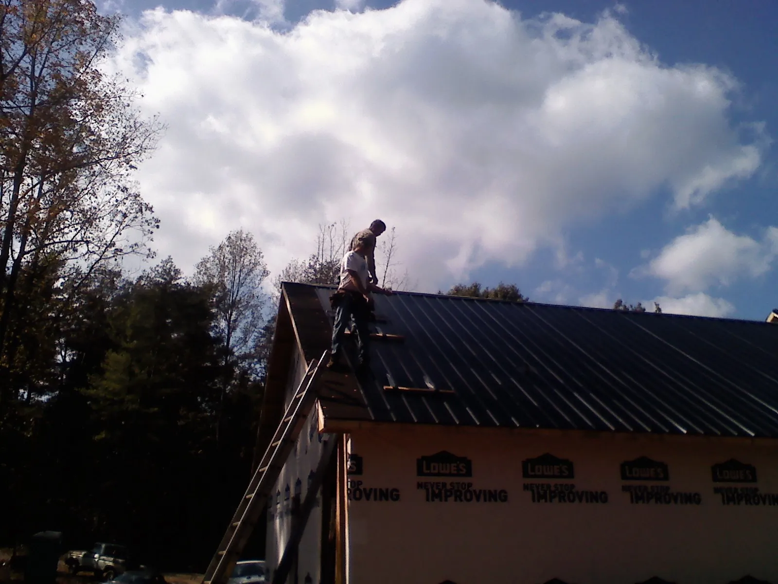 Roofer fastening dark metal panels high against a cloudy sky, from a Roof Inspection job in Saint Hedwig