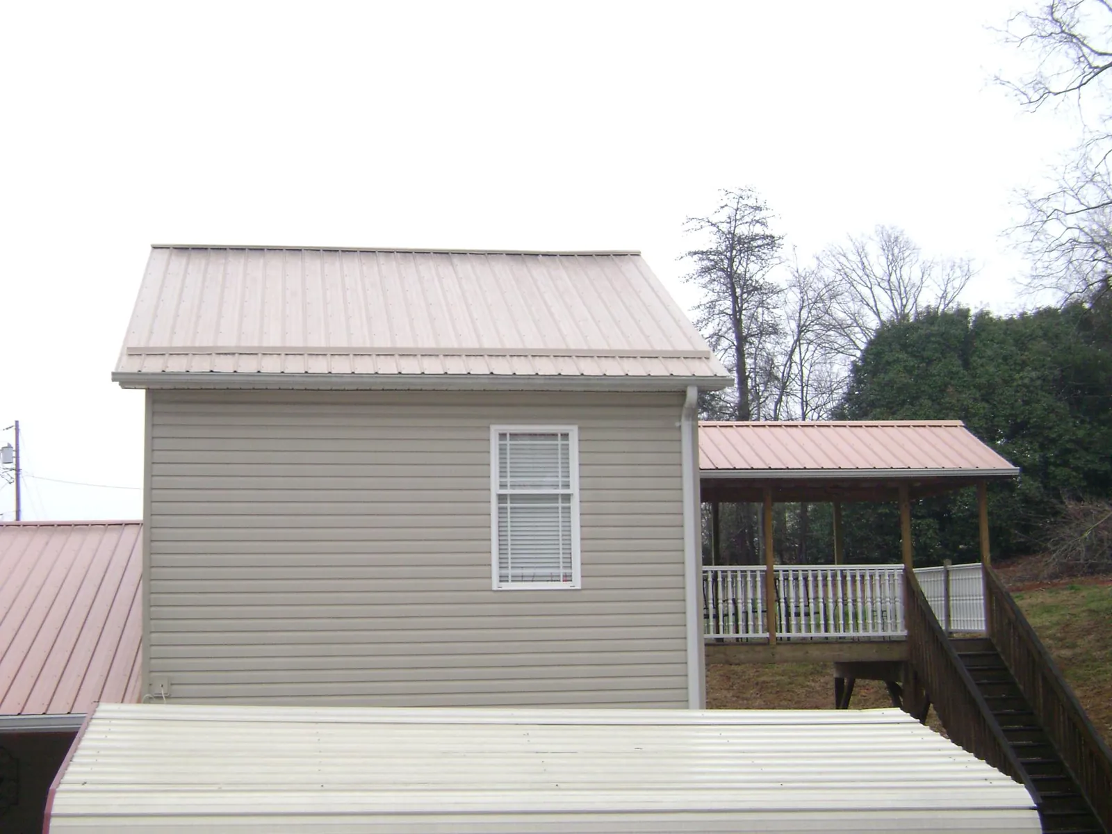 Tan metal roofs on a two story addition and attached porch, from a Roof Replacement job in Saint Hedwig